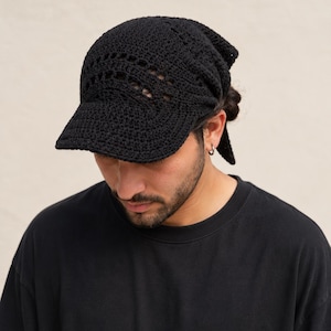 Può includere: Un berretto all'uncinetto nero caratterizzato da una visiera strutturata e un intricato motivo traforato sulla corona. Il copricapo è realizzato in filato con una trama visibile e include lacci sul retro per una vestibilità regolabile.