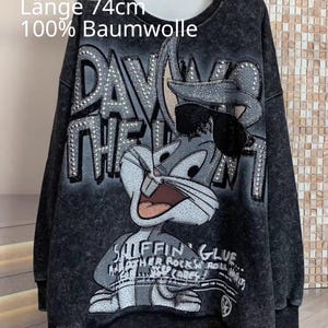 Könnte beinhalten: Ein anthrazitfarbenes Sweatshirt im Acid-Wash-Look mit einem strassbesetzten Bugs-Bunny-Motiv mit Sonnenbrille. Der Text lautet "DAWGS THE" und "SNIFFIN GLUE". Einheitsgröße 46-50, 70cm Achselweite, 74cm Länge, 100% Baumwolle.