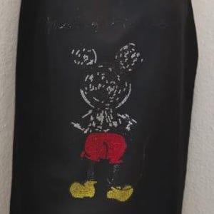 Könnte beinhalten: Schwarzer Schal mit einem gestickten Mickey Mouse-Design. Der Schal hat einen Fransenrand und eine Kapuze. Mickey Mouse ist mit roten Shorts, gelben Schuhen und einer weißen Umrandung dargestellt.