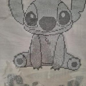 Könnte beinhalten: Hellgraues Bild der Figur Stitch aus dem Disney-Film Lilo & Stitch, hergestellt aus kleinen, funkelnden Verzierungen. Das Wort "Stitch!" steht darunter in demselben Material.