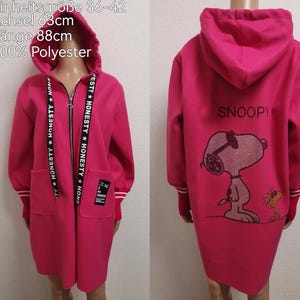 Könnte beinhalten: Ein magentafarbener Kapuzenmantel mit durchgehendem Reißverschluss und Taschen. Der Mantel hat den Text "HONESTY" auf dem Reißverschlussband und eine Snoopy-Grafik auf dem Rücken. Der Mantel ist 88 cm lang.