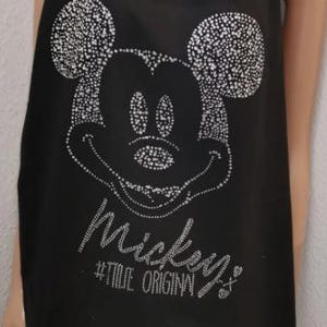 Könnte beinhalten: Schwarzer Schal mit einem funkelnden Mickey Mouse-Design. Die ikonische Figur ist in weißen, gepunkteten Verzierungen dargestellt. Der Schal hat einen Fransenboden und den Text "Mickey's #TRUE ORIGINAL".