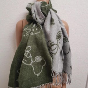 Könnte beinhalten: Wendescharf mit Snoopy-Design. Eine Seite ist olivgrün mit weißen Snoopy-Umrissen, die andere grau mit einem ähnlichen Design. Der Schal hat Fransen an den Enden.