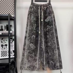 Könnte beinhalten: Weit geschnittene Jeanshose in verwaschenem Schwarz mit einem sich wiederholenden Muster aus Zeichentrickfiguren. Die Hose hat einen elastischen Bund mit weißem Kordelzug, ausgefranste vertikale Nähte und ist mit verstreuten Strasssteinen besetzt.