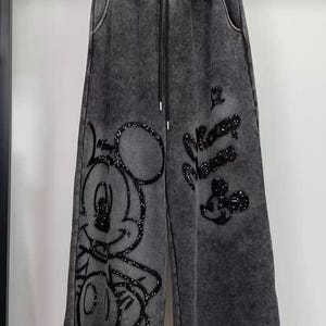 Könnte beinhalten: Weit geschnittene Hose aus dunkelgrauem Acid-Wash-Stoff mit elastischem Bund und schwarzem Kordelzug. Auf der Vorderseite befindet sich ein großes, schwarz paillettiertes Mickey-Mouse-Motiv auf dem linken Bein und der Schriftzug Mickey Mouse rechts.