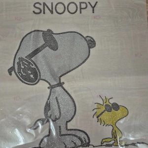 Könnte beinhalten: Dekoratives Design mit Snoopy und Woodstock, verziert mit glitzernden Strasssteinen. Das Wort "SNOOPY" ist oben abgebildet. Snoopy wird in sitzender Position mit Sonnenbrille dargestellt, mit Woodstock daneben.