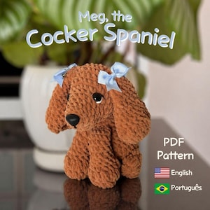 Könnte beinhalten: Ein gehäkelter Cocker Spaniel Hund in Brauntönen, mit schwarzen Augen und Nase sowie zwei hellblauen Schleifen. Der Text "Meg, the Cocker Spaniel" befindet sich über dem Hund. Das Bild enthält auch den Text "PDF Pattern" und Flaggen für Englisch und Portugiesisch.