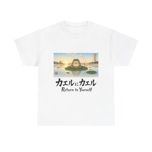 以下が含まれることがあります： 穏やかな池のハスの葉の上にいるカエルの穏やかなイラストが特徴の白いTシャツ。アートワークには日本語のテキストと英語のフレーズ「Return to Yourself」が含まれています。デザインはTシャツの中央に配置されています。