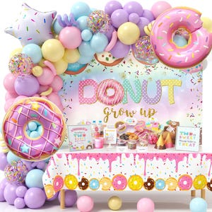 May include: A colorful donut-themed party decoration set. Includes a backdrop with the words "Donut grow up", donut-shaped balloons, and a table with a donut-patterned tablecloth. Balloons are pink, purple, yellow, and blue.