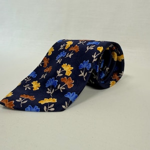 Könnte beinhalten: Eine dunkelmarineblaue Krawatte mit einem sich wiederholenden Muster aus kleinen, stilisierten Blumen in den Farben leuchtendes Gelb, kräftiges Blau und gedämpftes Braun, mit dünnen, hellen Stielen und Blättern zwischen den Blüten.