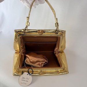 May include: A metallic gold handbag with a single top handle and a metal frame closure. The interior is lined with brown satin and contains a matching small coin purse. A white circular tag attached to the bag reads After Five COCKTAIL BAGS by LOWY & MUND.