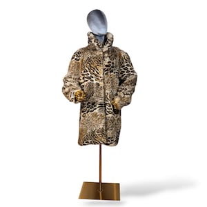 May include: A long-sleeved coat featuring a textured faux fur material with a brown, tan, and black animal print pattern. The coat has a high collar, a straight silhouette, and is displayed on a mannequin stand with a gold-colored base.