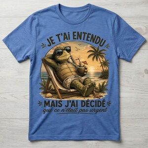 May include: Blue t-shirt with a graphic of a turtle relaxing on a beach chair, wearing sunglasses and holding a drink. The image includes text in French: "JE T'AI ENTENDU MAIS J'AI DÉCIDÉ que ce n'était pas urgent."