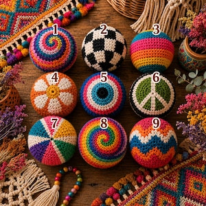Puede incluir: Nueve bolas de ganchillo coloridas con varios diseños, incluyendo una espiral, un patrón de balón de fútbol, rayas, una flor, un ojo, un signo de la paz y un patrón en zigzag. Las bolas están dispuestas sobre una superficie de madera con textiles decorativos y flores secas.