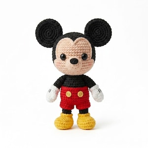 May include: A handmade crochet Mickey Mouse doll. The doll has black ears, a black body, red shorts with yellow buttons, yellow shoes, and white gloves. The face is tan with black eyes and a black nose.