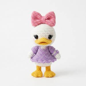 May include: Crocheted Daisy Duck doll with a pink bow, white head, and a purple dress. The doll has yellow feet and a yellow beak. The doll has black eyes and eyelashes. The doll is standing on a white surface.