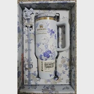 May include: A white Stanley Quencher tumbler with a blue floral pattern, a handle, and a matching straw in a box. The tumbler features the text Stanley, LoveShackFancy, and The Flowstate Quencher Tumbler 1.18 L. The box has a matching floral print.