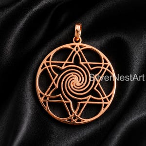 May include: A rose gold pendant with a circular design featuring a six-pointed star and a central spiral. The pendant has a loop at the top for a chain. The background is a black, textured fabric.