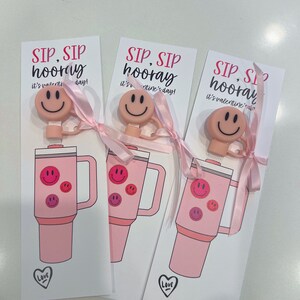 May include: Three pink Valentine's Day gift tags with the text "SIP, SIP hooray it's valentine's day!" and a pink smiley face charm attached to a pink ribbon. Each tag features a pink tumbler with a smiley face design.