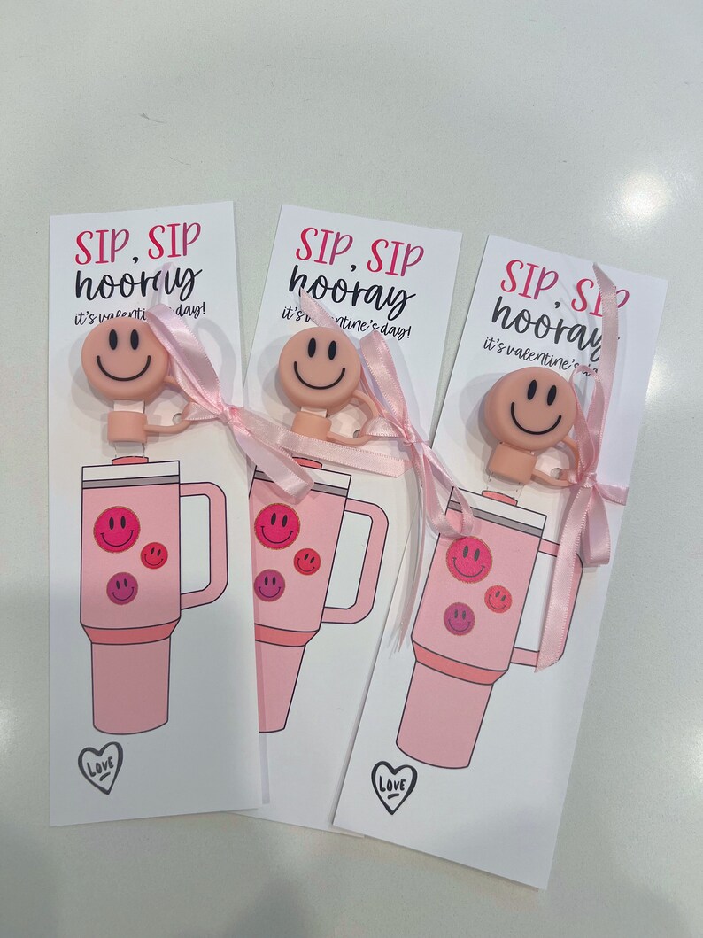 May include: Three pink Valentine's Day gift tags with the text "SIP, SIP hooray it's valentine's day!" and a pink smiley face charm attached to a pink ribbon. Each tag features a pink tumbler with a smiley face design.
