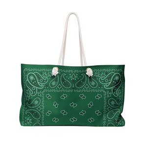 May include: A dark green tote bag featuring a white paisley bandana pattern. The bag has two white rope handles attached with silver-toned metal grommets. The design includes intricate teardrop-shaped paisley motifs and small floral accents.