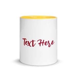 Puede incluir: Una taza de cerámica blanca con el interior y el borde de color amarillo brillante. El exterior presenta las palabras Text Here escritas en una fuente cursiva de color rojo oscuro centrada en la parte frontal. La taza tiene un cuerpo liso.
