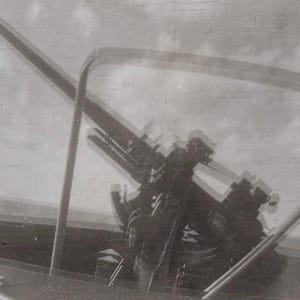 May include: Vintage black and white photograph of a large artillery gun, possibly an anti-aircraft gun, mounted on a platform. The gun is angled upwards, suggesting it's ready to fire. The image has a grainy texture.