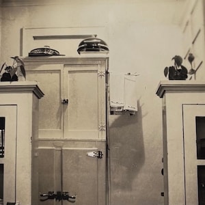 Puede incluir: Una cocina vintage con armarios blancos, puertas de cristal y una encimera de madera. Los armarios tienen un diseño decorativo en las puertas.