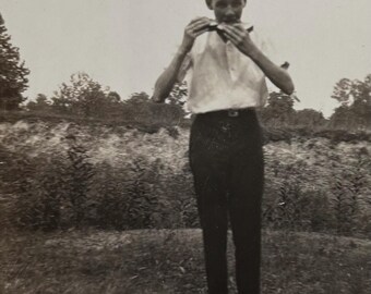 May include: A black and white photo of a person wearing a white shirt and dark pants, standing in a field and holding a small object in their hands.