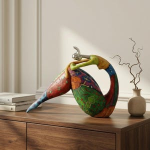 Puede incluir: Una escultura decorativa que presenta una figura estilizada y curva con una cabeza de plata metálica. El cuerpo está pintado en secciones vibrantes y multicolores de rojo, verde, azul y naranja, adornado con patrones geométricos.