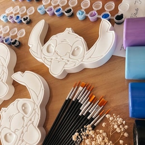 May include: A paint-by-number kit featuring a white Stitch character, paint pots in various colors, and paintbrushes. The kit includes a Stitch figure, paint pots, and brushes for a creative painting project. The paint pots are arranged in rows, with a variety of colors.