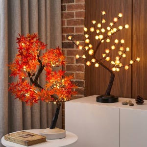 Peut inclure: Deux lampes décoratives LED en forme d'arbre. L'une présente des feuilles d'érable orange, l'autre des lumières sphériques. Les deux ont des branches et des bases marron foncé. L'arbre aux feuilles d'érable repose sur une base blanche, l'autre sur une base noire.