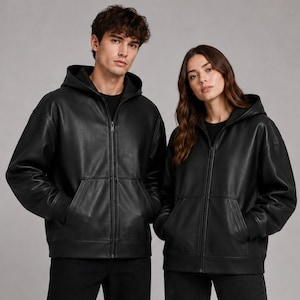 May include: Two identical black zip-up hoodies made of a smooth, leather-like material. Each hoodie features a front zipper closure, a hood, long sleeves with ribbed cuffs, and two front pockets. The garments are worn over simple black shirts.