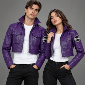 May include: Two matching cropped purple jackets with a high collar, front zipper, and two chest pockets. Each jacket features a circular black patch on the left sleeve with the white text CUSTOMIZE. The jackets are worn over plain white t-shirts.