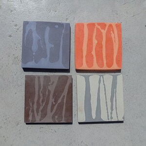 Può includere: Quattro sottobicchieri quadrati con un design unico. Ogni sottobicchiere presenta un colore diverso: grigio, arancione, marrone e grigio chiaro. Ogni sottobicchiere ha un motivo di linee verticali in una tonalità più chiara del colore di base.