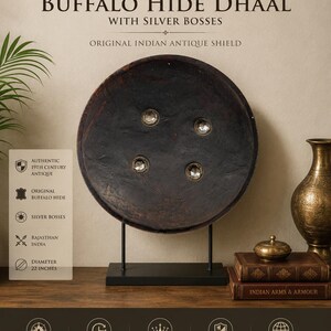 May include: A 19th-century buffalo hide Dhaal, an original Indian antique shield, with silver bosses. The shield is round, dark brown, and mounted on a black stand. Diameter is 22 inches.