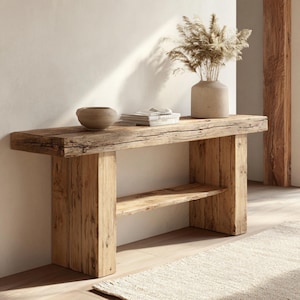 Puede incluir: Una consola rústica de madera con una balda inferior. La mesa está hecha de madera recuperada, mostrando la veta y textura naturales. Un jarrón de cerámica con plantas secas, un cuenco pequeño y libros están sobre la mesa. La mesa mide 152 cm de largo.