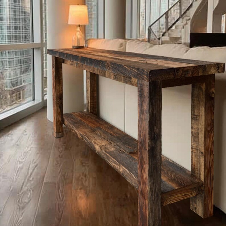 Op de afbeelding: Een rustieke, rechthoekige consoletafel van gerecycled hout. De tafel heeft een onderste plank en een verweerde afwerking met verschillende bruintinten. De tafel is ongeveer 152 cm lang.