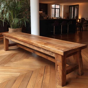 May include: A long, rectangular wooden bench with a natural finish. The bench has thick legs and a sturdy frame, showcasing the wood's grain. The design is rustic and suitable for indoor use. The bench is approximately 183 cm long.