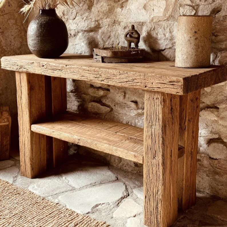Op de afbeelding: Een rustieke houten console met een onderste plank. De tafel is gemaakt van gerecycled hout en heeft een natuurlijke, verweerde uitstraling. Een donkere vaas met gedroogde planten en andere decoratieve items staan op het tafelblad. De tafel is 122 cm lang, 41 cm breed en 76 cm hoog.