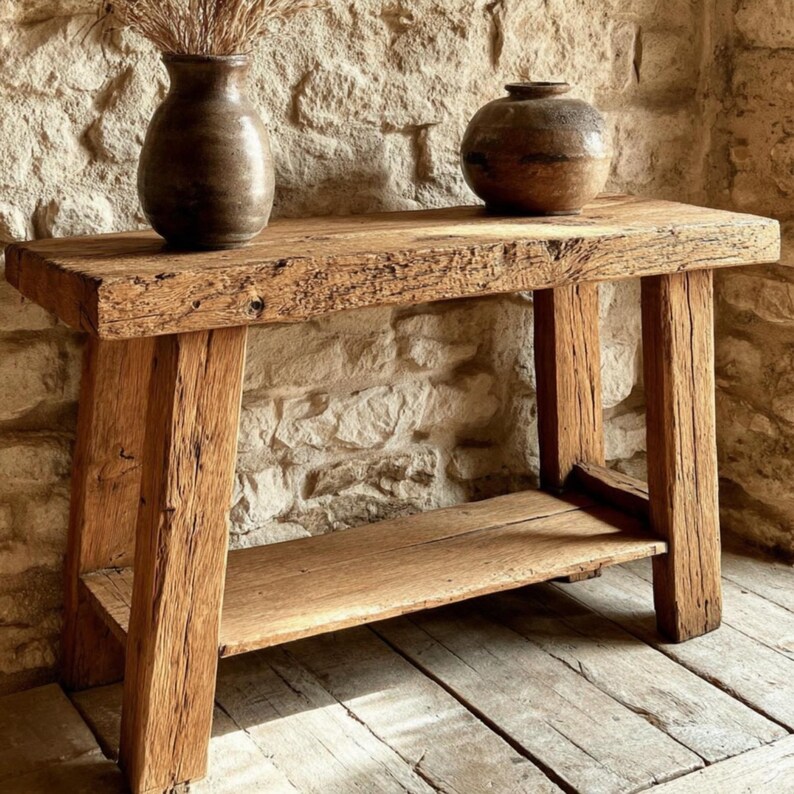 Op de afbeelding: Een rustieke houten console tafel met een onderste plank en vier stevige poten. De tafel is gemaakt van gerecycled hout, dat de natuurlijke nerf en textuur laat zien. Twee keramische vazen staan bovenop.