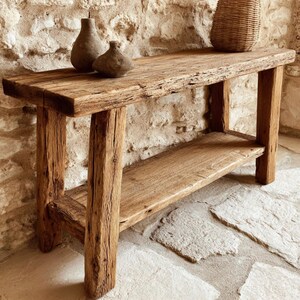 Op de afbeelding: Een rustieke houten console met een onderste plank. De tafel is gemaakt van gerecycled hout en toont natuurlijke nerf en textuur. Twee kleine, donkerbruine vazen en een geweven mand staan op het tafelblad. Afmetingen: ongeveer 152 cm lang, 41 cm breed en 76 cm hoog.