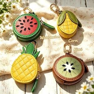 Peut inclure: Quatre porte-monnaie en forme de fruits et légumes avec des fermoirs en métal doré. L'ensemble comprend une pastèque ronde rouge et verte, un épi de maïs jaune, un ananas jaune avec des feuilles vertes et un kiwi rond marron et vert, tous zippés.