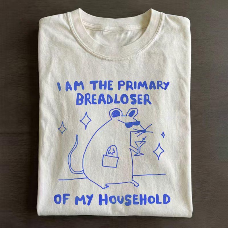 May include: Cream-colored t-shirt with a blue graphic of a mouse wearing sunglasses and holding a cocktail. The text reads "I AM THE PRIMARY BREADLOSER OF MY HOUSEHOLD."