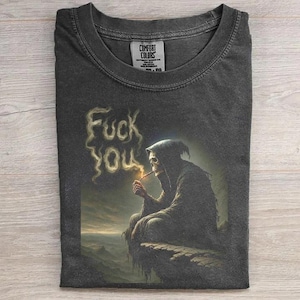 May include: Dark gray t-shirt featuring a grim reaper smoking a cigarette, with the words "Fuck You" spelled out in smoke. The shirt is from Comfort Colors.