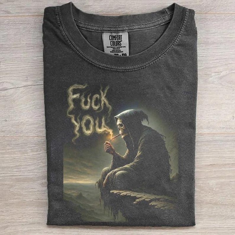 May include: Dark gray t-shirt featuring a grim reaper smoking a cigarette, with the words "Fuck You" spelled out in smoke. The shirt is from Comfort Colors.