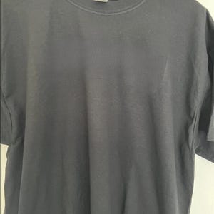 May include: A dark gray t-shirt hanging on a wooden hanger. The short-sleeved shirt has a crew neck and a tag at the back of the neck. The fabric appears to be a soft cotton blend.