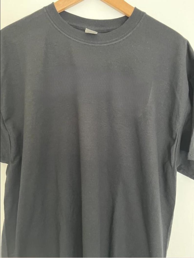May include: A dark gray t-shirt hanging on a wooden hanger. The short-sleeved shirt has a crew neck and a tag at the back of the neck. The fabric appears to be a soft cotton blend.