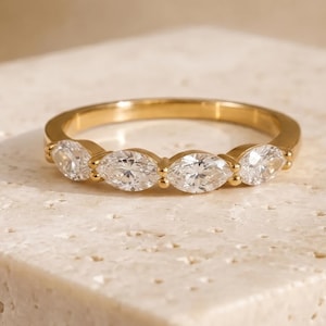 May include: A gold band ring featuring four marquise-cut clear stones set in a row. The ring has a polished yellow gold finish and the stones are arranged horizontally along the top half of the band, secured by small gold prongs.