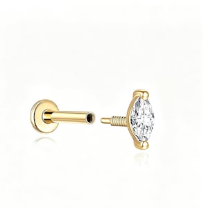 May include: A gold flat back labret stud earring featuring a marquise-cut clear gemstone. The piece consists of a threaded post with a circular base and a separate top attachment with a pointed, elongated stone set in a gold metal frame.